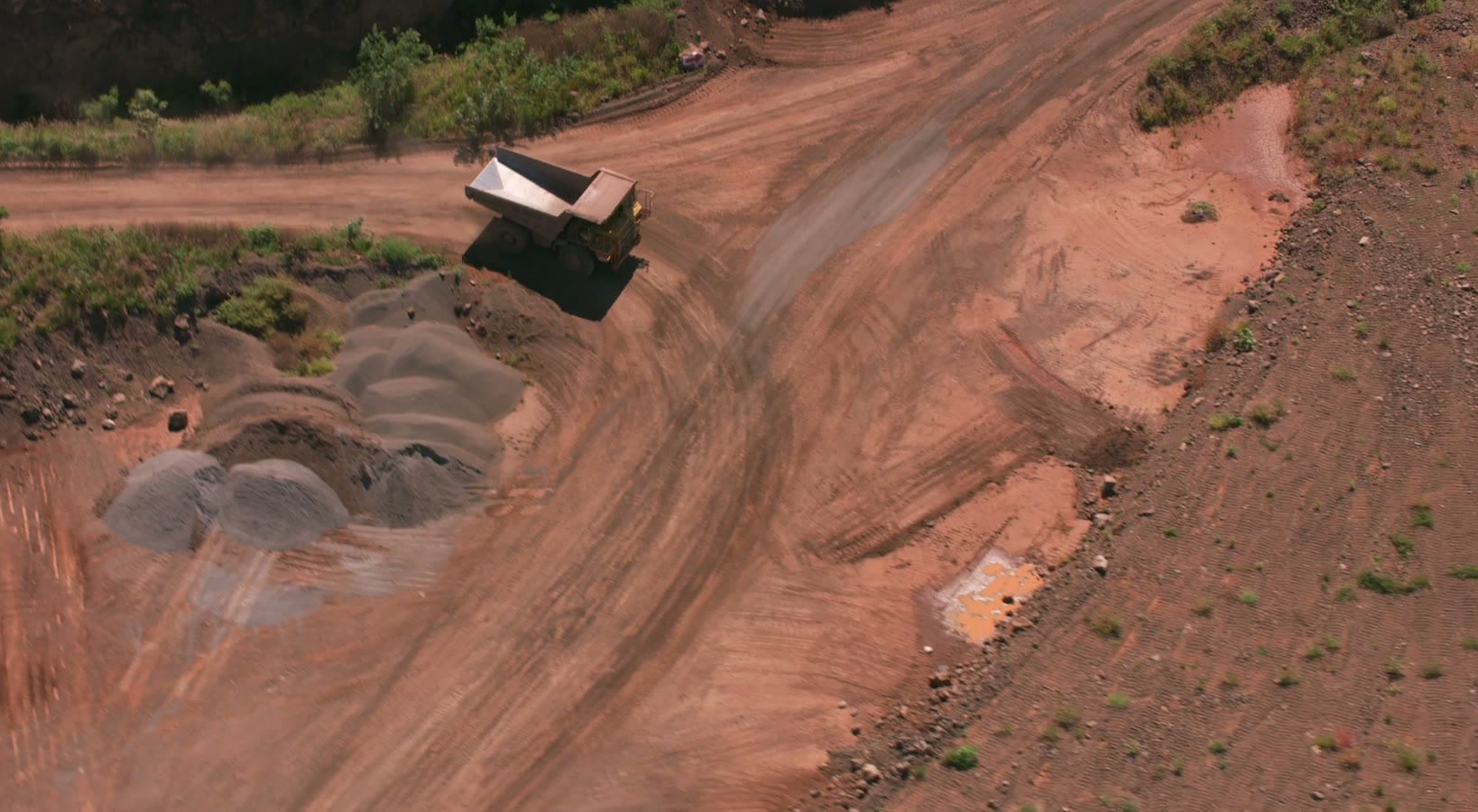 Haul truck climbing a red-dirt road past copper-ore stockpiles