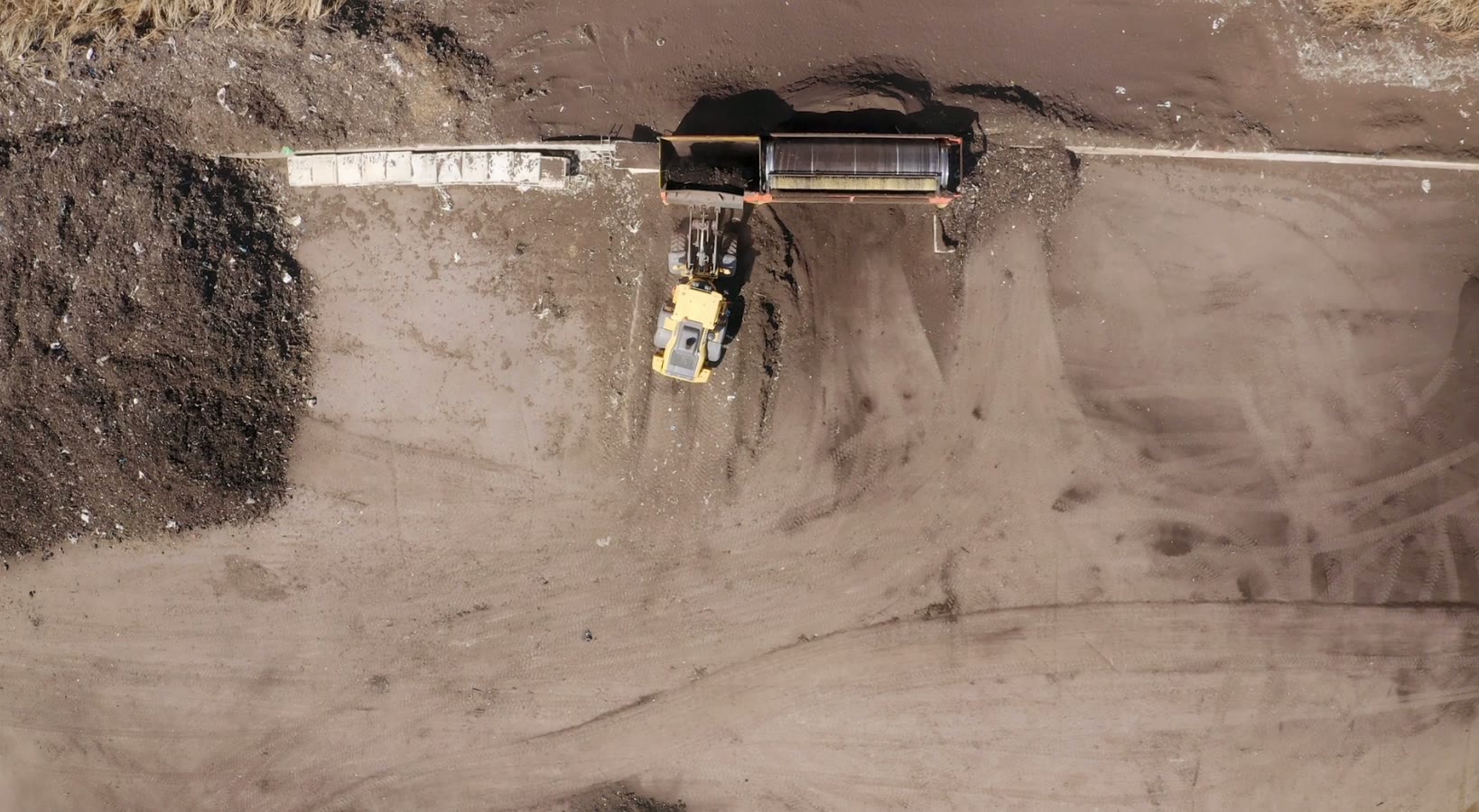 Aerial view of a wheel loader feeding a bulk truck at a stockyard